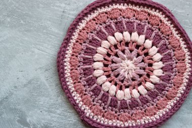 Pembe organik iplikten örülmüş trivet. Gri arkaplanda el yapımı tığ tutacağı ve metin için boşluk. 