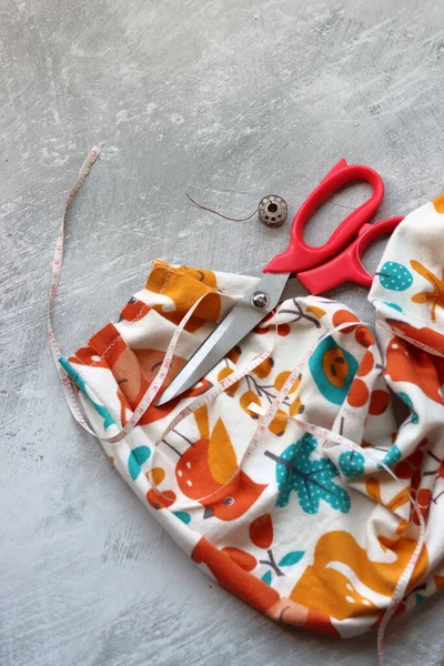 Yumuşak flanel kumaştan bir elbise dikmek, işlem aşamasında. Fotokopi alanı olan gri bir arka planda dikiş aletleri ve aksesuarları dikiyorum. Hobiler ve el sanatları konsepti. 