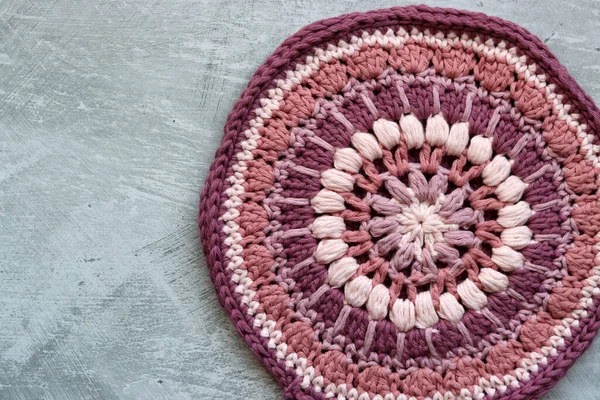 Pink and purple round crochet pattern on light grey textured background with copy space. Close up photo of hand made trivet or potholder.