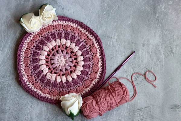 Pink and purple round crochet pattern on light grey textured background with copy space. Close up photo of hand made trivet or potholder.