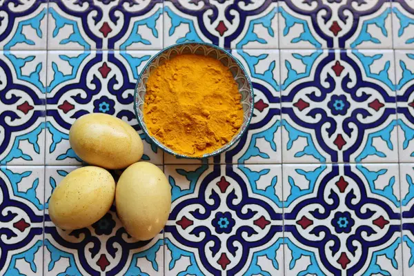 Natural dye for Easter eggs. Turmeric powder and eggs in a bowl on a blue background with copy space.