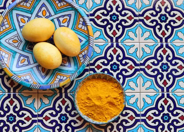Natural dye for Easter eggs. Turmeric powder and eggs in a bowl on a blue background with copy space.