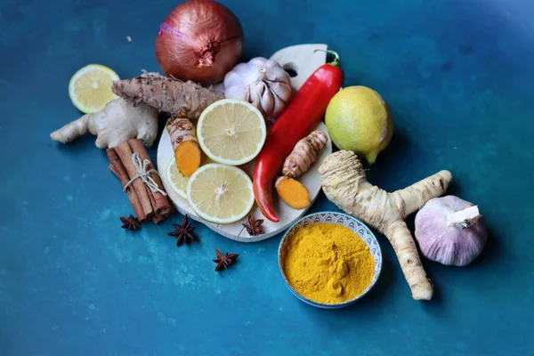 Ginger, lemon, turmeric, cinnamon sticks, anise star, garlic bulb, horseradish on a blue background with copy space. Cold and flu season concept.