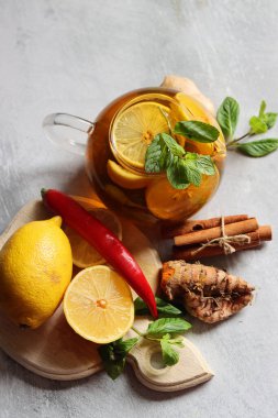 Zencefilli çay, limon, zerdeçal kökü ve gri zemin üzerinde nane şekeri ve metin için yeri olan cam çaydanlık. Soğuk algınlığı ve grip mevsimi. 