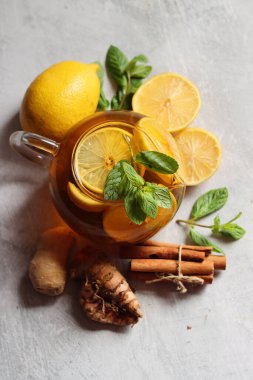 Zencefilli çay, limon, zerdeçal kökü ve gri zemin üzerinde nane şekeri ve metin için yeri olan cam çaydanlık. Soğuk algınlığı ve grip mevsimi. 