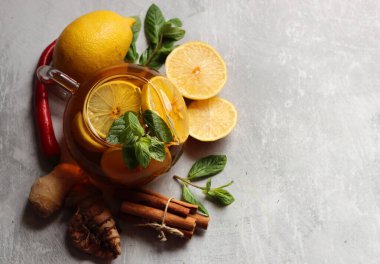 Zencefilli çay, limon, zerdeçal kökü ve gri zemin üzerinde nane şekeri ve metin için yeri olan cam çaydanlık. Soğuk algınlığı ve grip mevsimi. 