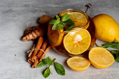 Zencefilli çay, limon, zerdeçal kökü ve gri zemin üzerinde nane şekeri ve metin için yeri olan cam çaydanlık. Soğuk algınlığı ve grip mevsimi. 