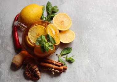 Zencefilli çay, limon, zerdeçal kökü ve gri zemin üzerinde nane şekeri ve metin için yeri olan cam çaydanlık. Soğuk algınlığı ve grip mevsimi. 