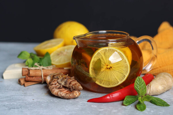 Чайник с горячим чаем, имбирь, куркума корень, корица палочки, лимон и мята листья на сером фоне с копировальным пространством. Рецепт противовоспалительного зимнего напитка. 
