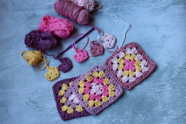 Büyükanne örgü örme işlemini tamamlıyor. Renkli Afgan kareleri, yakın plan fotoğraf. Kopyalama alanı olan gri arkaplan.  