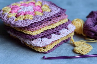 Büyükanne örgü örme işlemini tamamlıyor. Renkli Afgan kareleri, yakın plan fotoğraf. Kopyalama alanı olan gri arkaplan.  