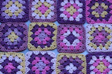 El yapımı tığ işi arka plan. Açık gri masada renkli büyükanne kareleri. 