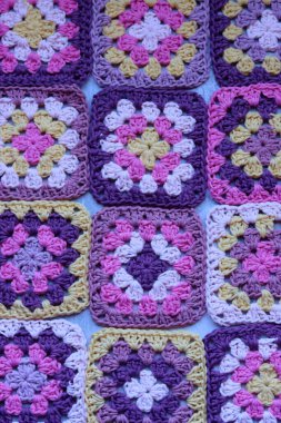 El yapımı tığ işi. Tığ işi pembe, mor, sarı ve beyaz büyükanne kareleri. Güzel desen, yakın plan fotoğraf. Yumuşak pamuk ipliği dokusu. Metin için alanı olan gri arkaplan. 