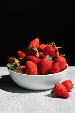 Beyaz masa örtüsündeki bir kasede çilekler siyah bir arkaplan ve metin için yer var.. 