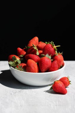 Beyaz masa örtüsündeki bir kasede çilekler siyah bir arkaplan ve metin için yer var.. 