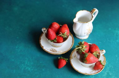 Turkuaz arka planda klasik porselen bardaklarda çilek ve metin için yer var. Güzel yaz meyveleri. Yakın çekim.. 