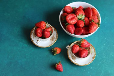 Turkuaz arka planda klasik porselen bardaklarda çilek ve metin için yer var. Güzel yaz meyveleri. Yakın çekim.. 