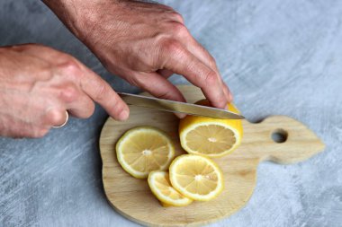 Tahta kesme tahtasıyla limon kesen bir adamın ellerine yakın çekim. Limonata hazırlığı devam ediyor. 