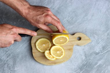 Tahta kesme tahtasıyla limon kesen bir adamın ellerine yakın çekim. Limonata hazırlığı devam ediyor. 