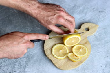 Tahta kesme tahtasıyla limon kesen bir adamın ellerine yakın çekim. Limonata hazırlığı devam ediyor. 