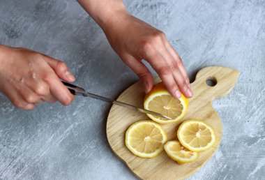 Dişi eller, gri arka planda tahta bir tahtada limon kesiyor ve yazı yazmak için yer açıyor.