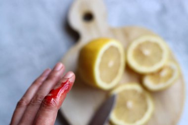 Kadın kazara parmağını kesti. Kadının elinde gerçek kan var. Dişi eller, gri arka planda tahta bir tahtada limon kesiyor ve yazı yazmak için yer açıyor.