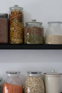Mutfak kilerinde stoklanmış. Beyaz arka planda kavanozlarda farklı tahıl gevrekleri olan raflar ve metin için yer var. Cam kaplarda farklı tohumlar ve tahıllar. Yiyecek depolama düzenlemesi. 