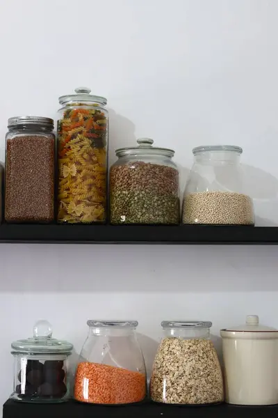 stock image Stocked kitchen pantry. Shelves with different cereals in jars on white wall background with space for text. Different seeds and cereals in glass containers. Food storage arrangement. 