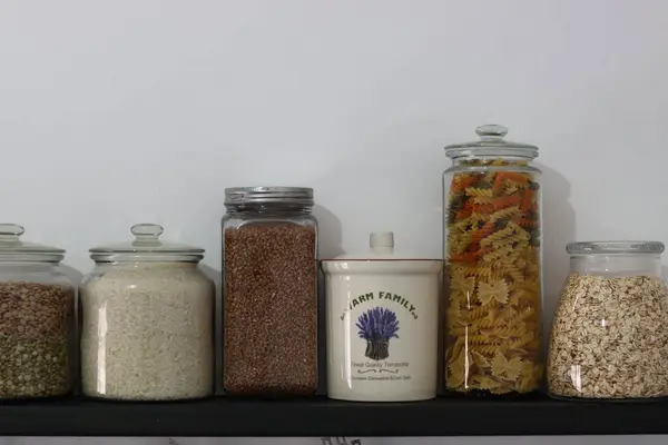 stock image Stocked kitchen pantry. Shelves with different cereals in jars on white wall background with space for text. Different seeds and cereals in glass containers. Food storage arrangement. 