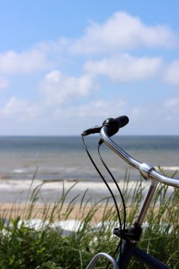 Hollanda plajı boyunca gezinti güvertesine parketmiş bisikletler. Mavi gökyüzü, sakin deniz suyu, arka planda kumlu plaj. Avrupa 'da yaz. 