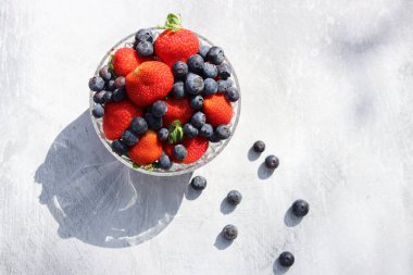 Cam bir kasede gri bir arka planda çilek ve yaban mersini. Mesaj için yer var. Taze konsept yemek. 