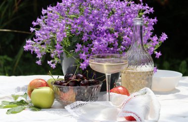 Bahçede yaz pikniği. Taze meyve, çiçek ve şampanya dolu beyaz bir masa örtüsü üzerinde. Bahçede sıcak bir gün. Romantik yemek masası.. 