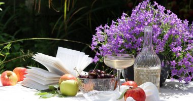 Yaz bahçesinde şarap, elma, kiraz ve çiçeklerle piknik masası. Mevsimlik meyve ve çiçeklerin güzel kompozisyonu. 