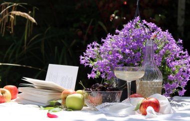 Bahçede yaz pikniği. Taze meyve, çiçek ve şampanya dolu beyaz bir masa örtüsü üzerinde. Bahçede sıcak bir gün. Romantik yemek masası.. 