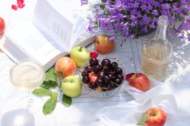Bahçede yaz pikniği. Taze meyve, çiçek ve şampanya dolu beyaz bir masa örtüsü üzerinde. Bahçede sıcak bir gün. Romantik yemek masası.. 