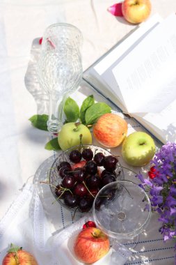 Yaz bahçesinde şarap, elma, kiraz ve çiçeklerle piknik masası. Mevsimlik meyve ve çiçeklerin güzel kompozisyonu. 