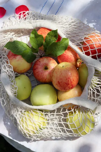stock image Green and red apples with leaves in white cotton mech bag. Eco friendly reusable shopping bag close up photo. Ripe apples in a string bag on a white tablecloth. Eating healthy concept. 