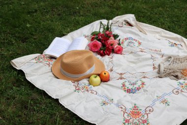 Bir buket çiçek, hasır şapka, yaz meyvesi ve piknik battaniyesinde açık bir kitap. Parkta romantik bir randevu. Yaz natürmort fotoğrafı. 