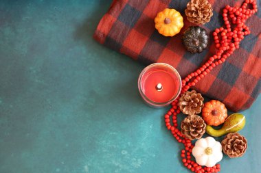 Balkabağı, köknar kozalakları, Rowan böğürtleninden yapılmış kırmızı tespih, yanan mum ve sıcak kırmızı ve gri ekose. Sonbahar havası hala hayat dolu. 