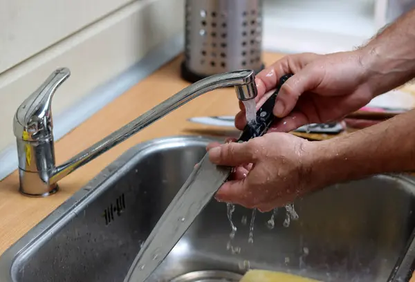 stock image Man washes a knife in kitchen sink 