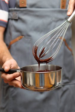 Şef çikolatalı pasta yapıyor, yakın plan el ele tutuşup tencereyi tutuyor. Çırpılmış çikolata. 