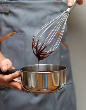 Şef çikolatalı pasta yapıyor, yakın plan el ele tutuşup tencereyi tutuyor. Çırpılmış çikolata. 