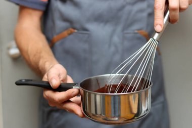 Şef çikolatalı pasta yapıyor, yakın plan el ele tutuşup tencereyi tutuyor. Çırpılmış çikolata. 