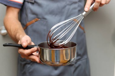Şef çikolatalı pasta yapıyor, yakın plan el ele tutuşup tencereyi tutuyor. Çırpılmış çikolata. 