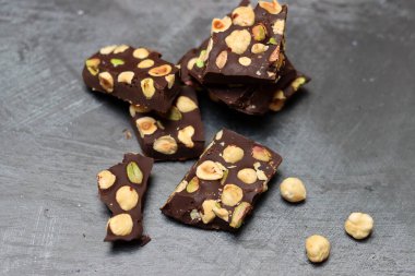 Fındıklı ev yapımı çikolata ve arka planda fıstık. Üzerinde fındık olan siyah çikolata parçaları. Gri arka plan, üst manzara, kopyalama alanı. Ev yapımı çikolata. Sağlıklı yeme kavramı. 