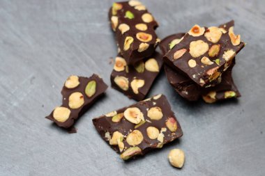 Fındıklı ev yapımı çikolata ve arka planda fıstık. Üzerinde fındık olan siyah çikolata parçaları. Gri arka plan, üst manzara, kopyalama alanı. Ev yapımı çikolata. Sağlıklı yeme kavramı. 