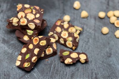 Fındıklı ev yapımı çikolata ve arka planda fıstık. Üzerinde fındık olan siyah çikolata parçaları. Gri arka plan, üst manzara, kopyalama alanı. Ev yapımı çikolata. Sağlıklı yeme kavramı. 