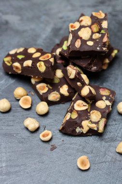 Fındıklı ev yapımı çikolata ve arka planda fıstık. Üzerinde fındık olan siyah çikolata parçaları. Gri arka plan, üst manzara, kopyalama alanı. Ev yapımı çikolata. Sağlıklı yeme kavramı. 