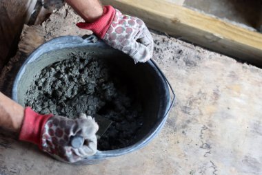 Eldivenli eller bir ev inşa etmek için çimento dolu bir kova tutuyor.