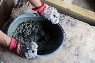 Eldivenli eller bir ev inşa etmek için çimento dolu bir kova tutuyor.